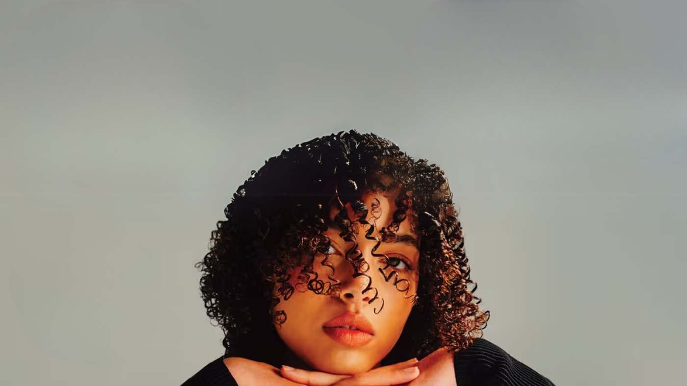 A woman with curly hair is seated on a chair, highlighting AG hair care products in the background.