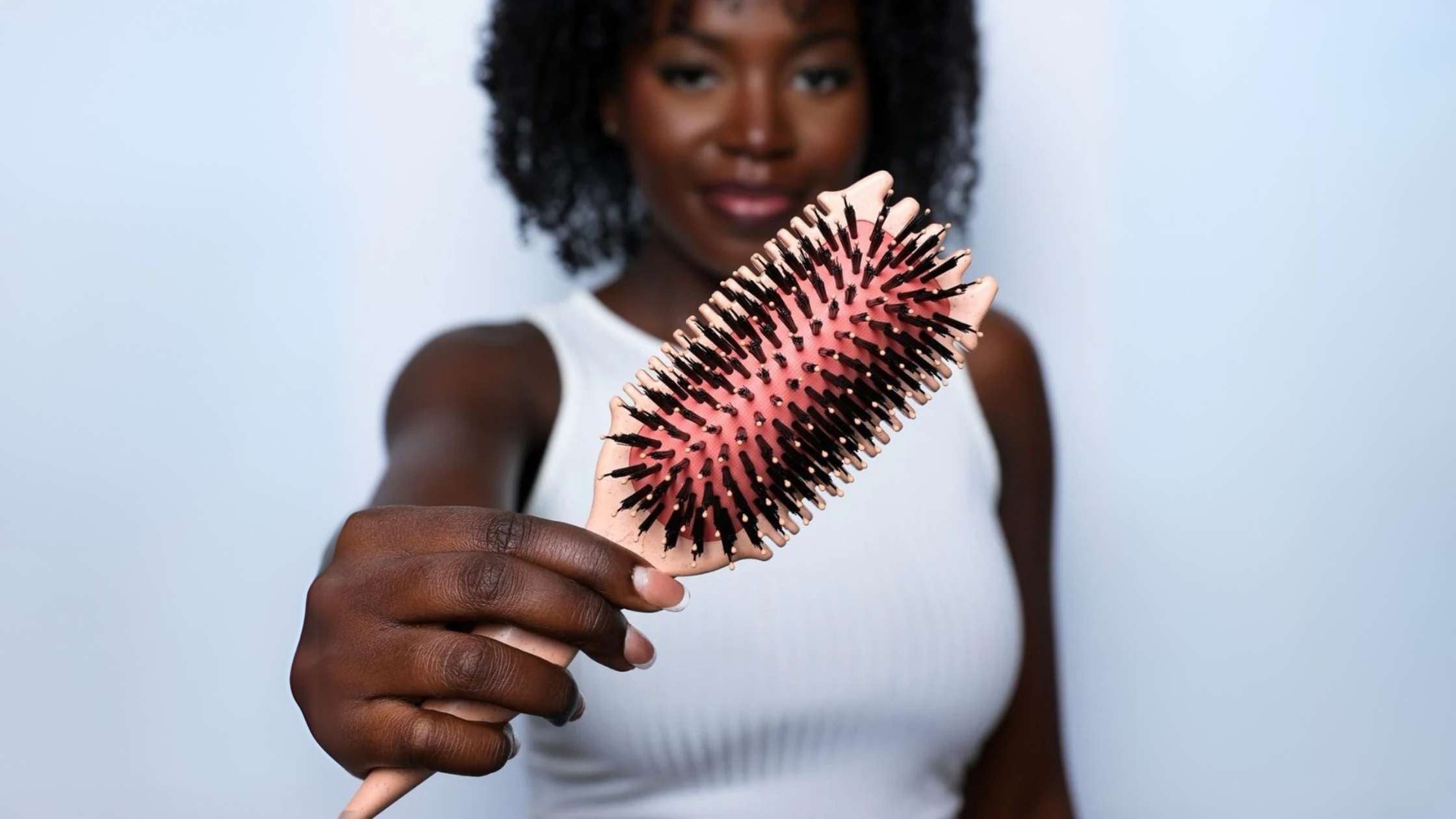 A woman with pink hair is holding a Volume EdgeLift Brush, highlighting her unique look and hair care routine.