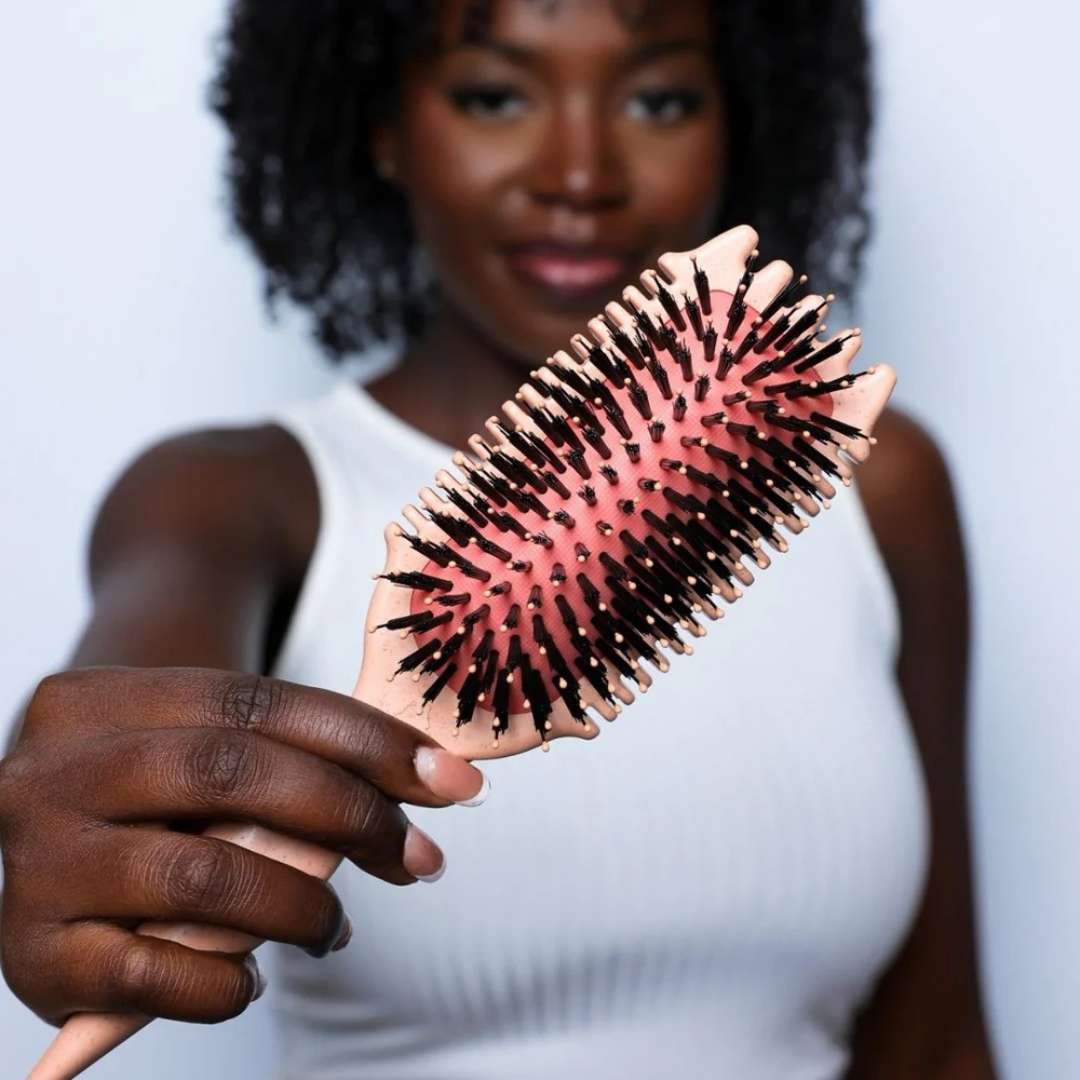 A woman with pink hair is holding a Volume EdgeLift Brush, highlighting her unique look and hair care routine.