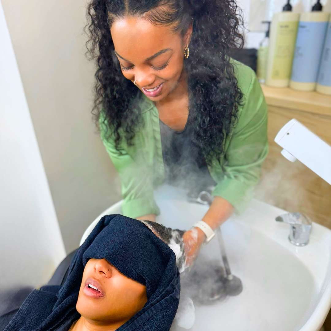 A woman with curly hair braids is having her hair washed in a sink at a salon.